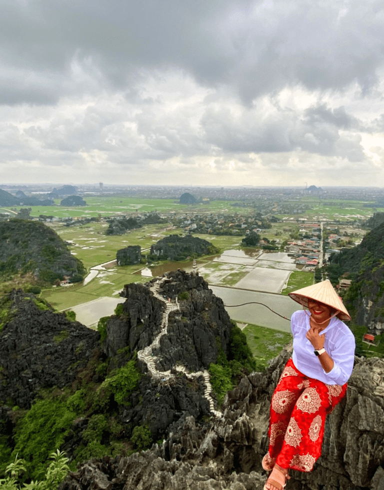 Una mujer sentada en las rocas escarpadas de la montaña Ngoa Long en las Cuevas de Mua, Vietnam. Las Cuevas de Mua. La mujer es la autora latina de este blog. Después de sobrevivir al cáncer, realizó una gira de victoria contra el cáncer en 2020 que fue cancelada después de un mes debido a la pandemia de COVID. Viajes en solitario para latinas como un acto de rebelión.