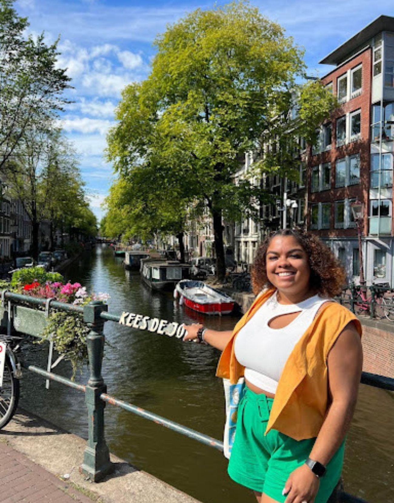 Una  Latina alegre posa a lo largo del pintoresco canal de Ámsterdam, rodeada de arquitectura tradicional holandesa y coloridas flores.