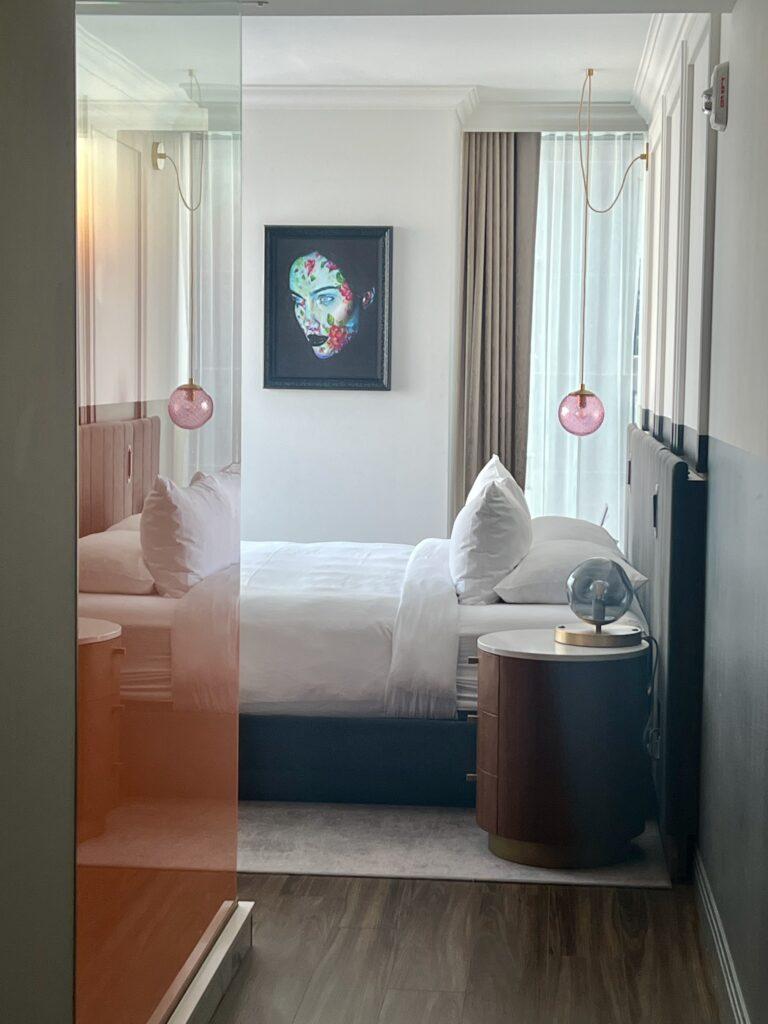 Guest room at HONEYROSE Hotel Montréal with pink blown-glass pendant light and framed portrait art, featured in The Queen of Trips guide on where to stay in Montréal 2026.